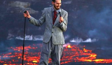 Image shows Ben Miller next to a live volcano with hot lava.