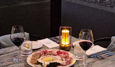 Image shows charcuterie and melted cheese platter with glasses of red wine.