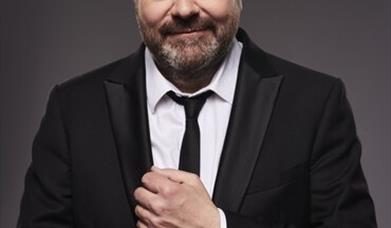 Image shows Hal Cruttenden in suit adjusting cufflinks and smiling at camera