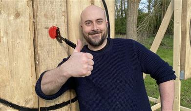 Man with a thumbs up next to axe target