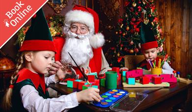 Two children dressed as elves painting with Father Christmas
